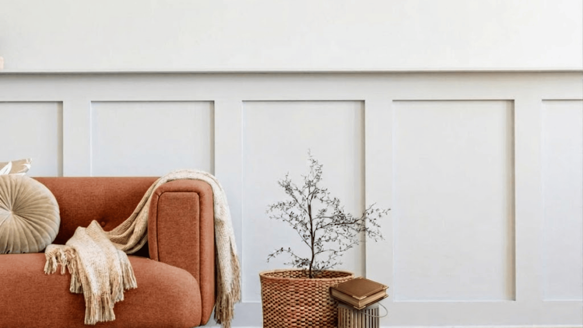 cozy living room corner with orange sofa throw blanket pillow and small plant beside wall paneling