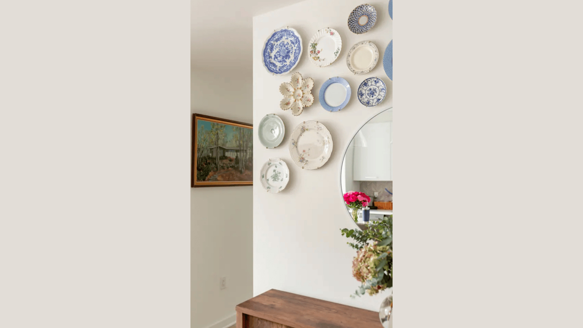 decorative plates arranged on kitchen wall above wooden table near round mirror