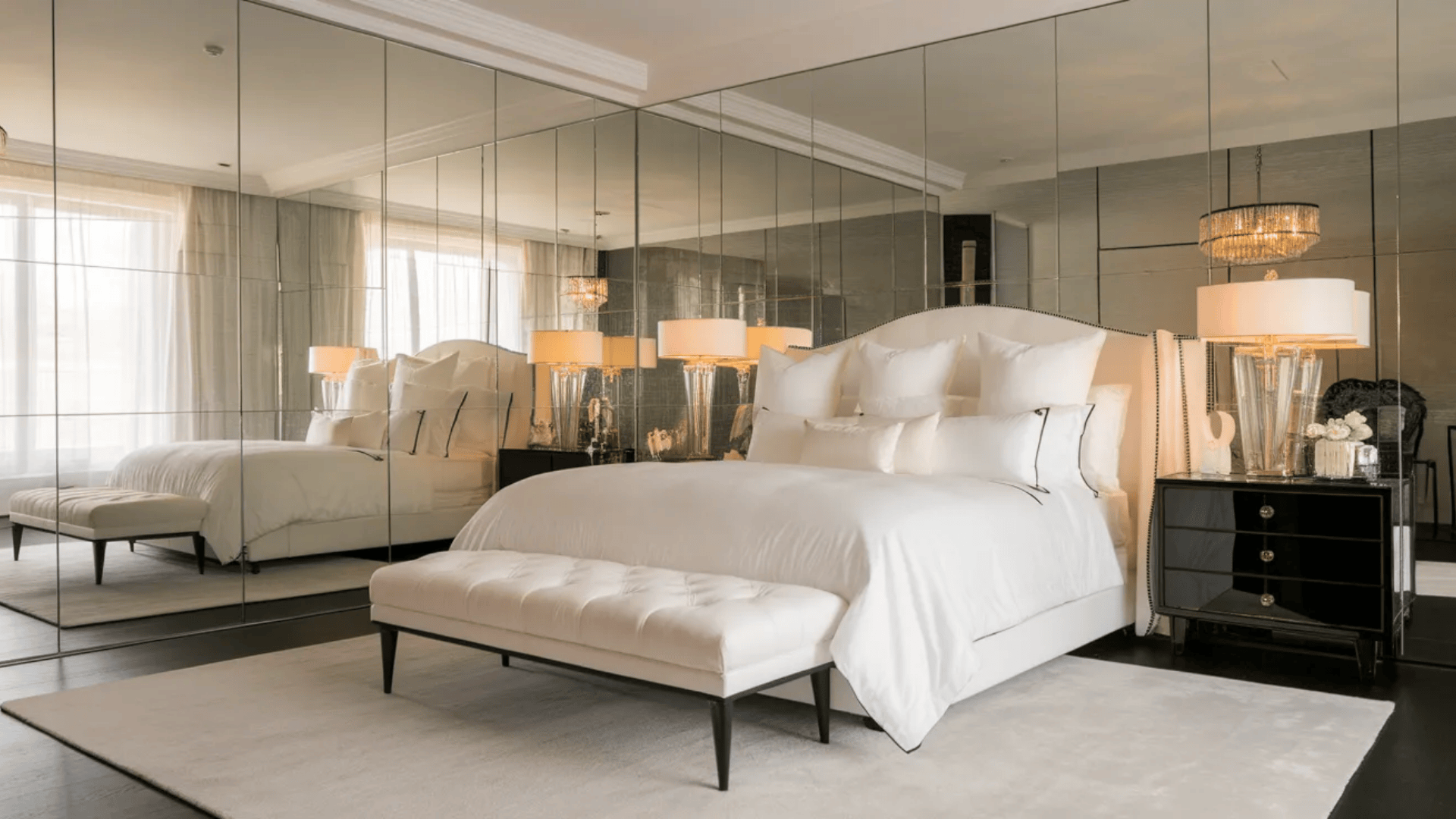 feminine black and white bedroom with mirrored wall plush bedding tufted bench black nightstand and decorative lamps