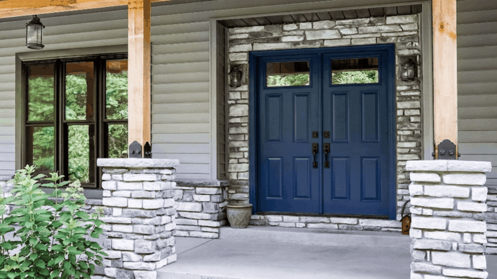 _front porch with double wooden entry doors stone door frame and gray siding exterior with pillars and steps
