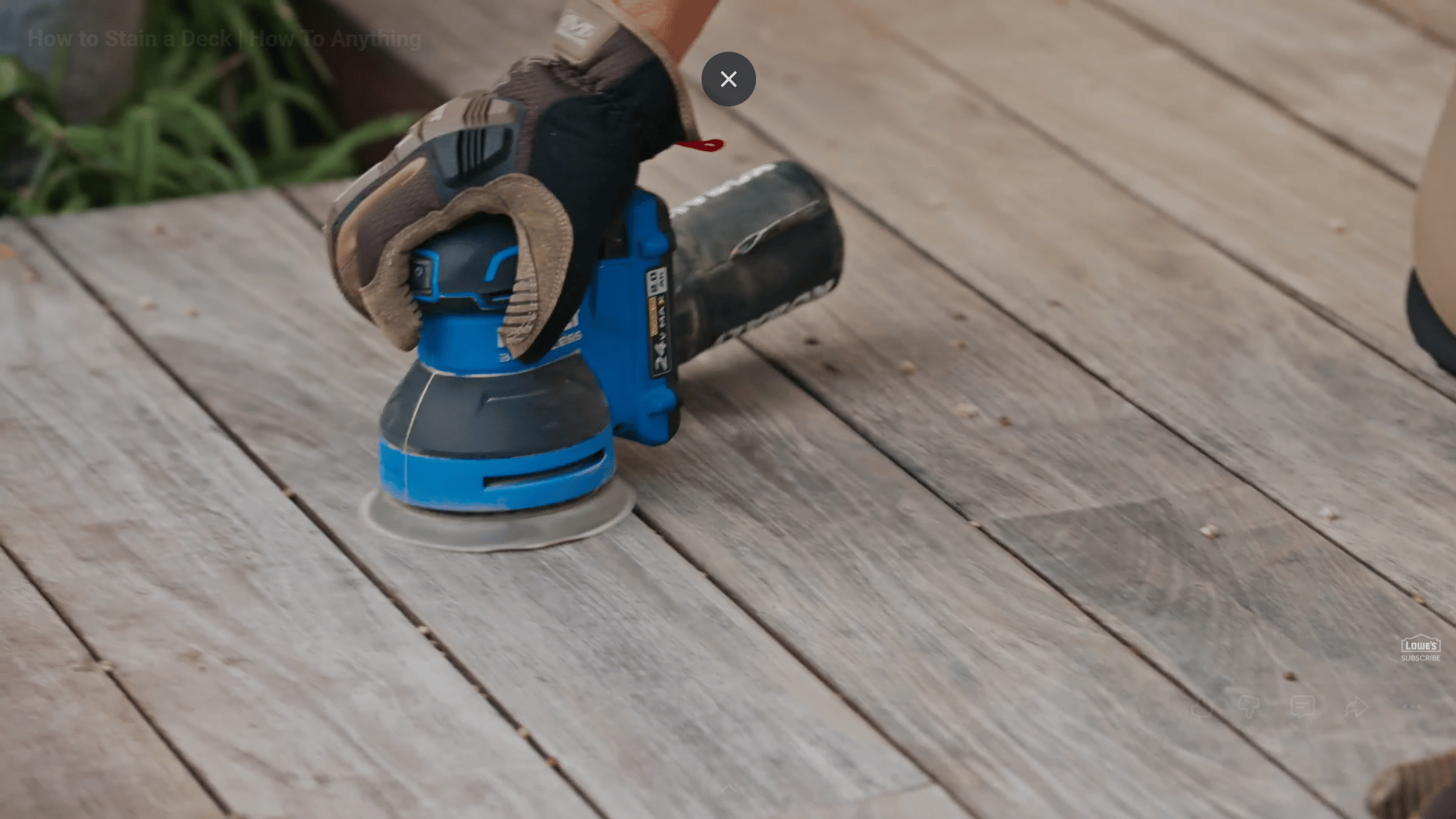 gloved hand using electric sander on weathered wooden deck surface during outdoor refinishing work