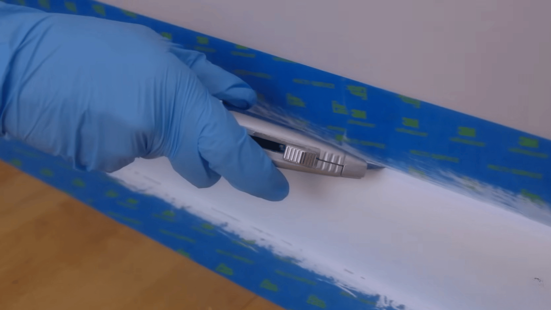 gloved hand using utility knife to carefully cut along taped painted edge for clean separation between wall and trim