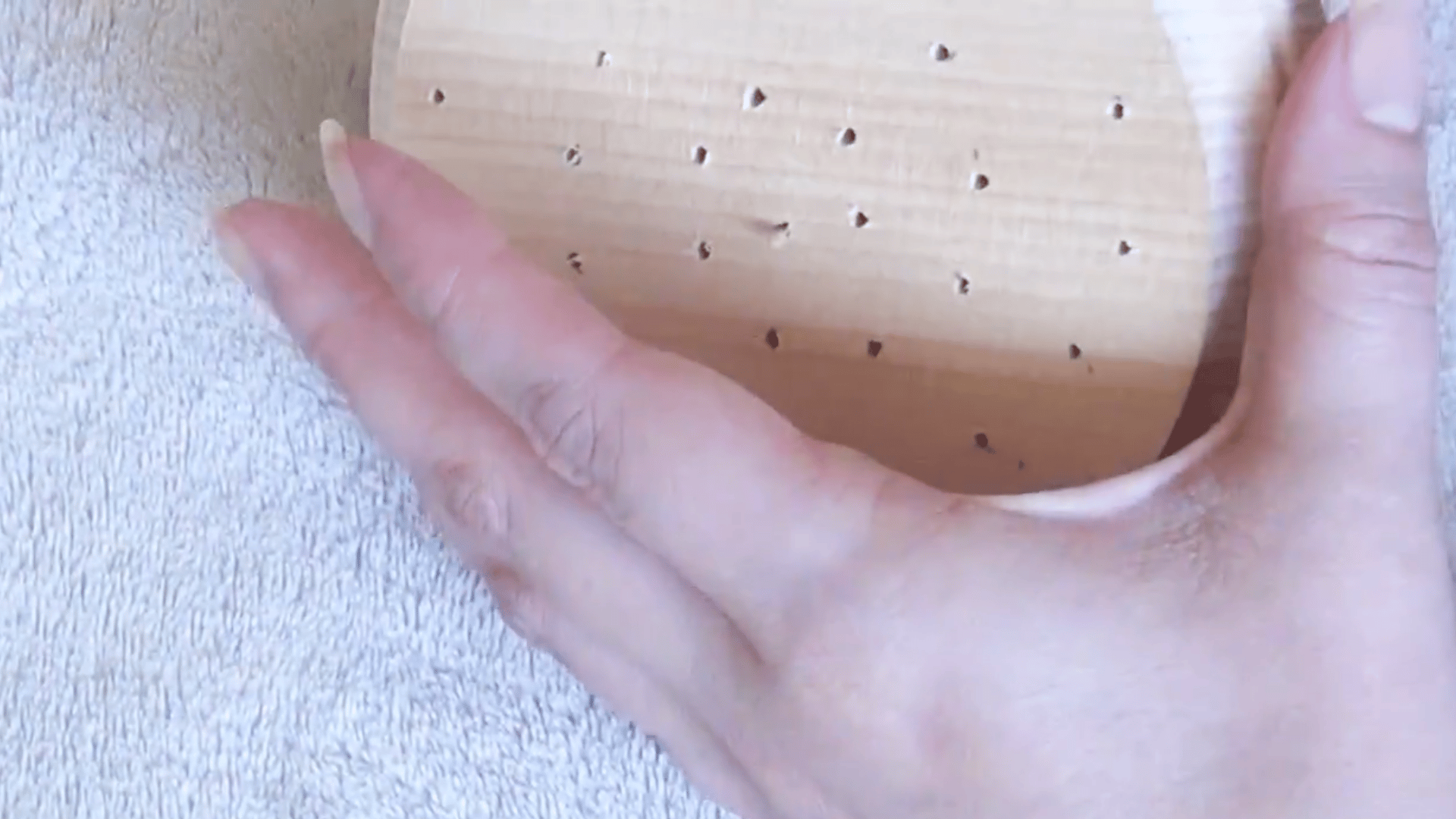 hand holding a wooden round with drilled holes prepared for a diy key wind chime craft project
