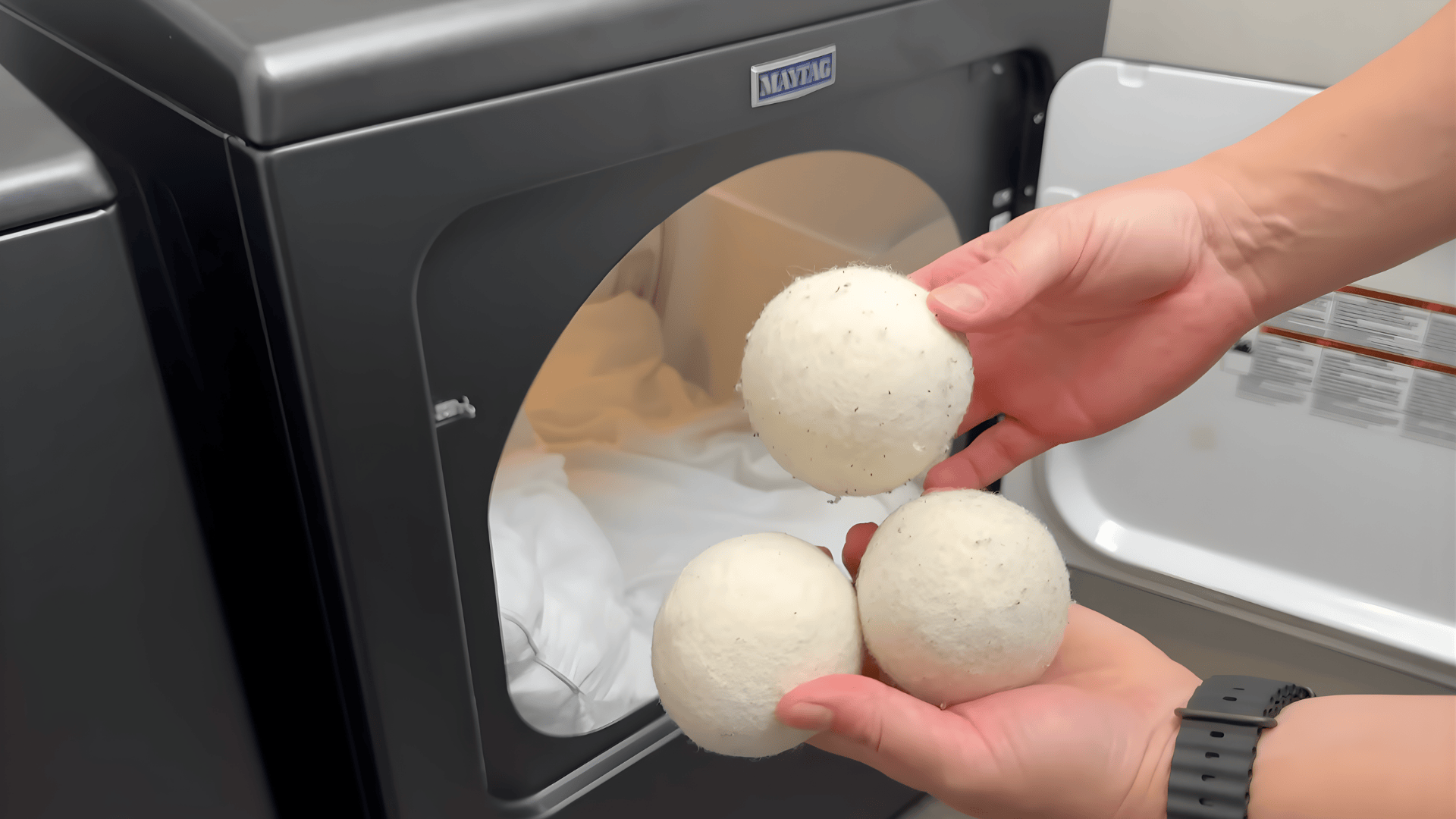 hand holding wool dryer balls in front of open dryer with pillow inside showing how to wash pillows can you wash pillows