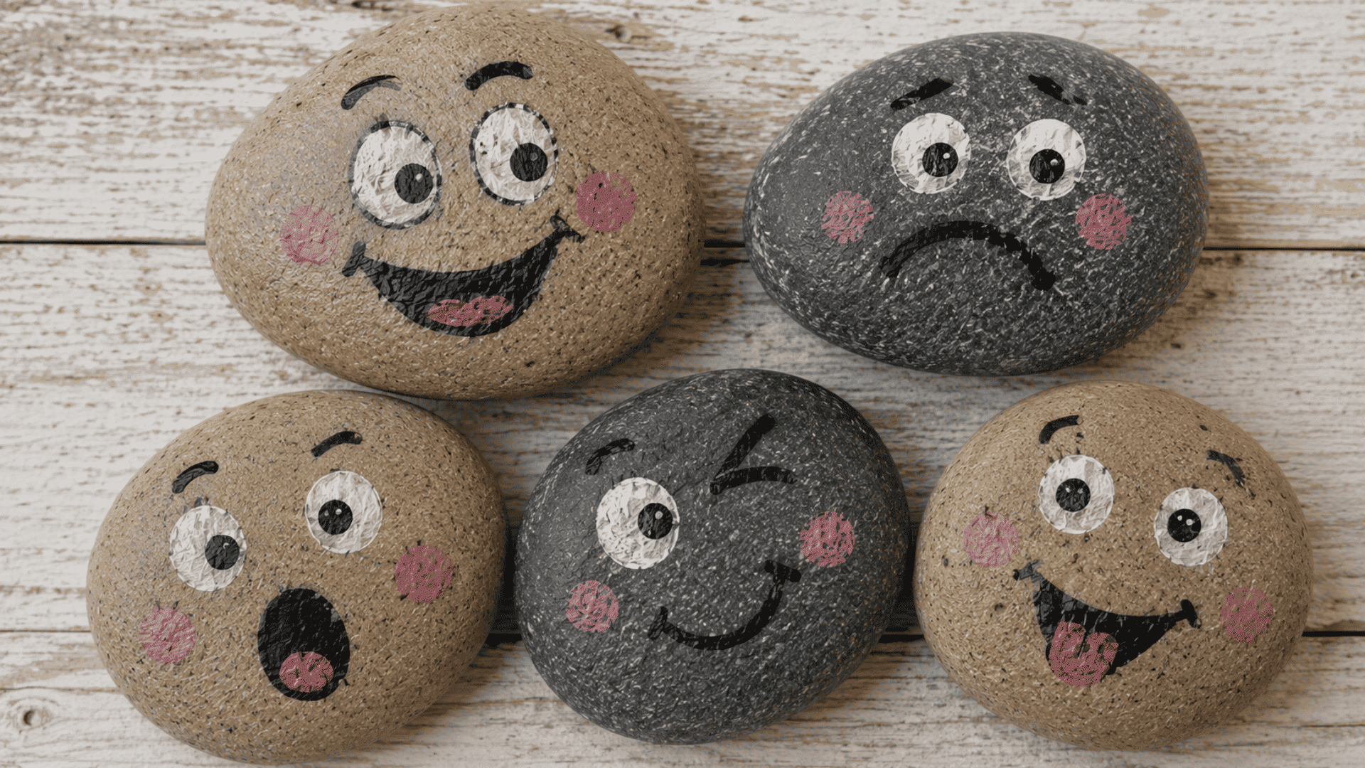 hand painted emoji faces on smooth stones with visible brush textures placed on rustic wooden surface