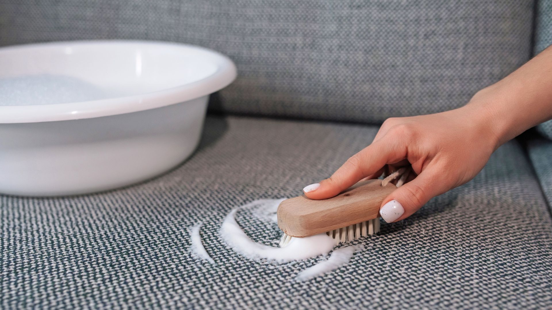 hand scrubbing a textured fabric surface with a small brush and soapy foam to remove dirt or stains from upholstery
