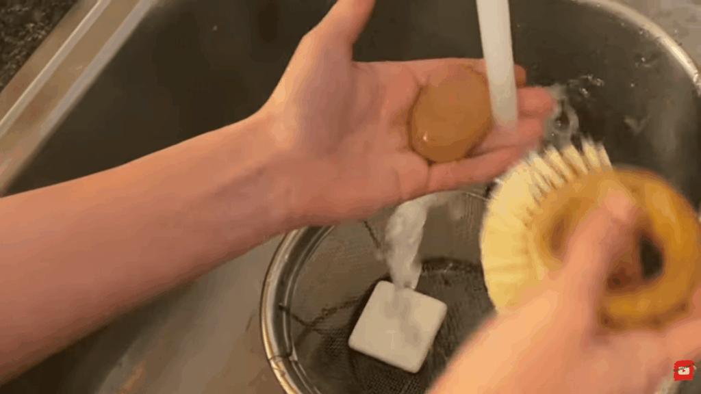 hands cleaning smooth rocks under running water in sink with brush and stone ready for painting