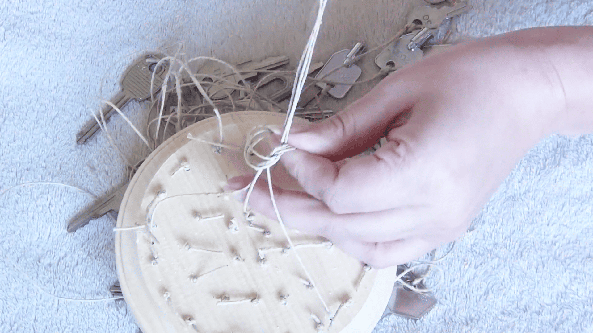 hands tying hanging strings together on a wooden key wind chime base with metal keys attached underneath