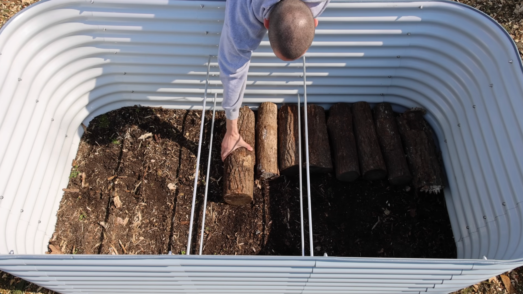 man placing logs in base layer showing how to layer a raised garden bed for better drainage and soil structure