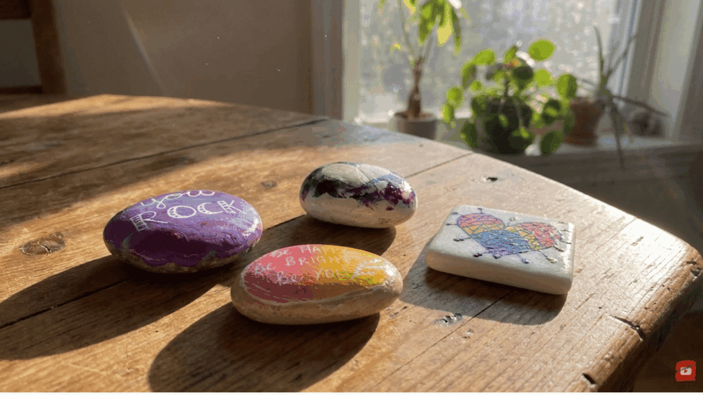 painted rocks with colorful words hearts and patterns placed on wooden table near sunny window and plants