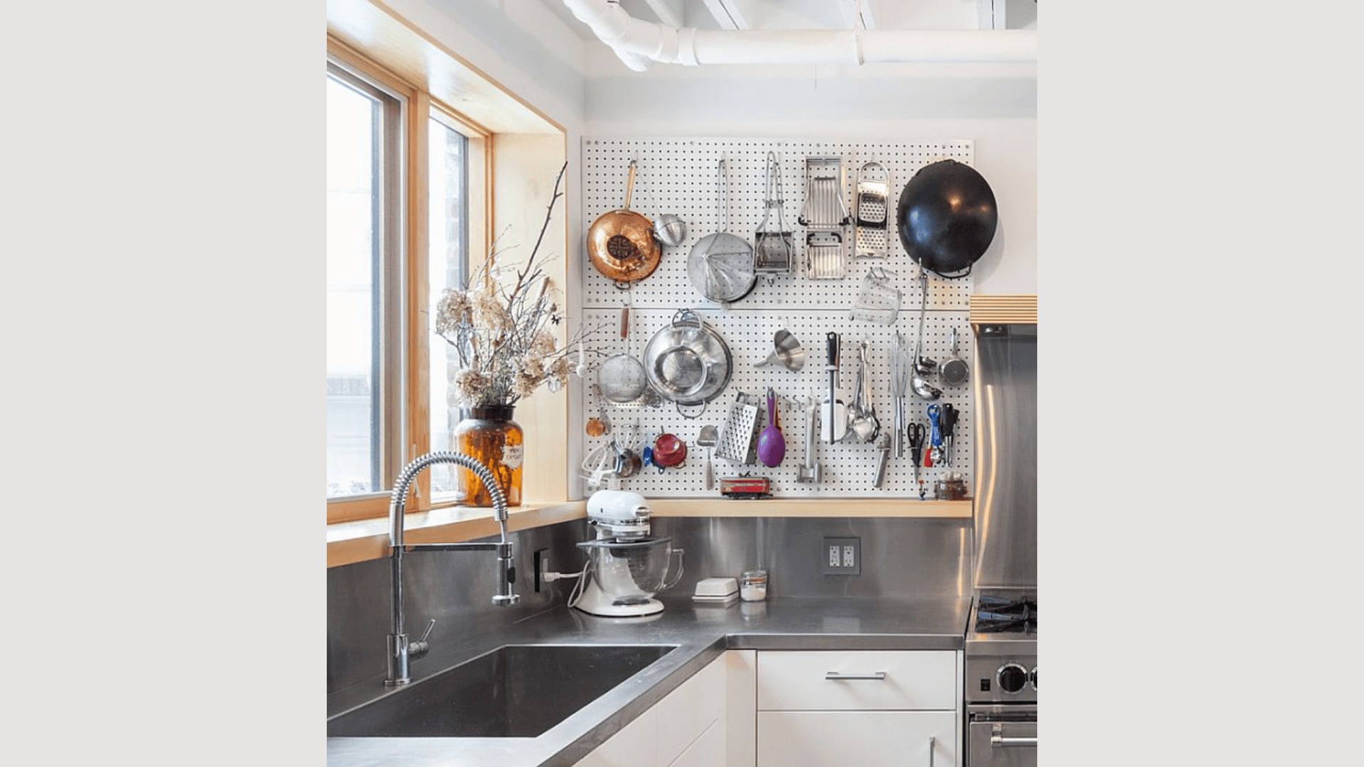 pegboard kitchen wall organizer with hanging pans utensils and tools above countertop