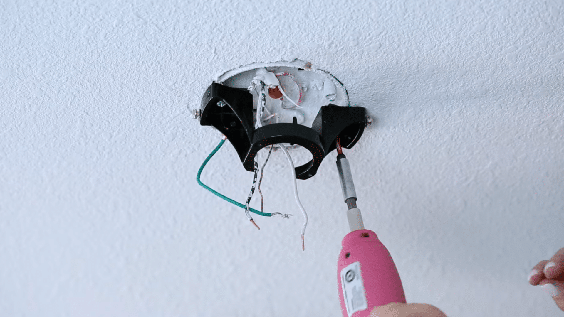 person attaching electrical wires to a white ceiling fan mount installed on an indoor ceiling during setup (1)