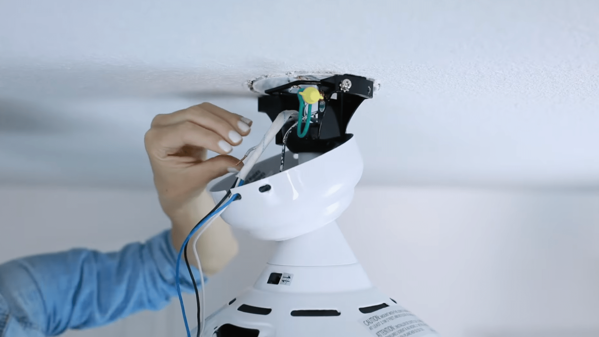 person connecting electrical wires to a ceiling fan mounting bracket during indoor ceiling fan installation