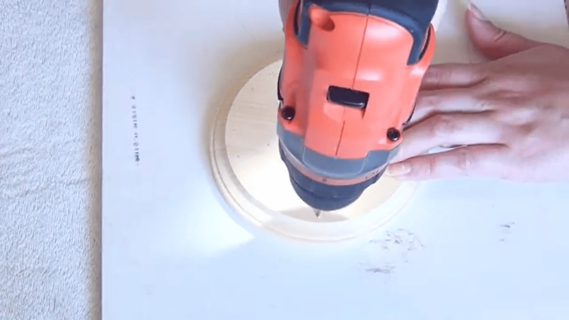 person drilling holes into a wooden round base for a diy key wind chime craft project at home