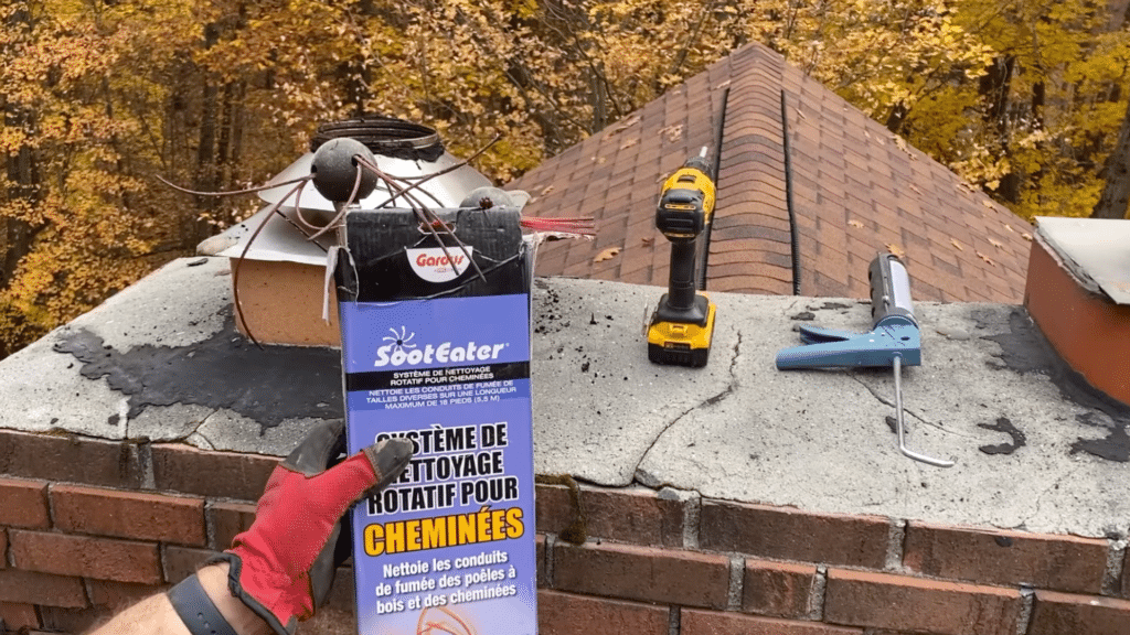 person holding chimney cleaning kit box on rooftop with drill sealant gun and chimney opening nearby