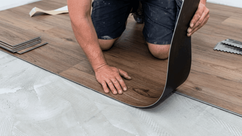 person installing wood look vinyl flooring over adhesive on a subfloor with plank flooring pieces nearby