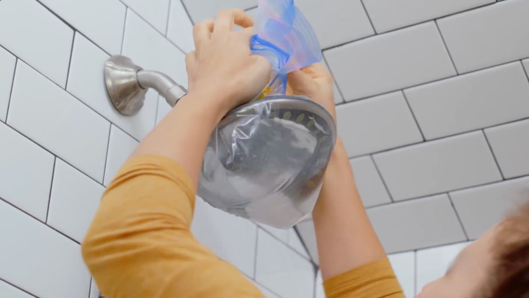 person places vinegar filled bag over shower head to remove hard water stains using a simple cleaning method