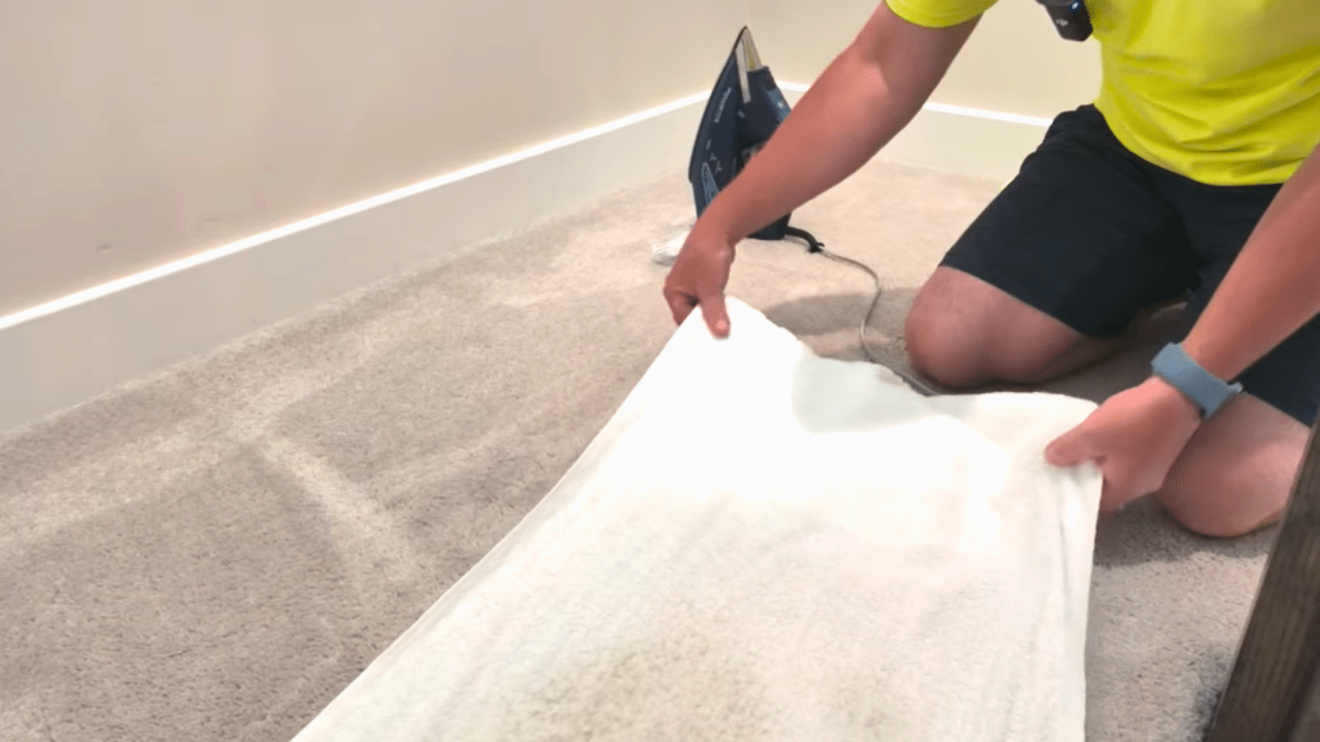 person pressing a white towel onto beige carpet to lift moisture and dirt from a treated stain after steaming