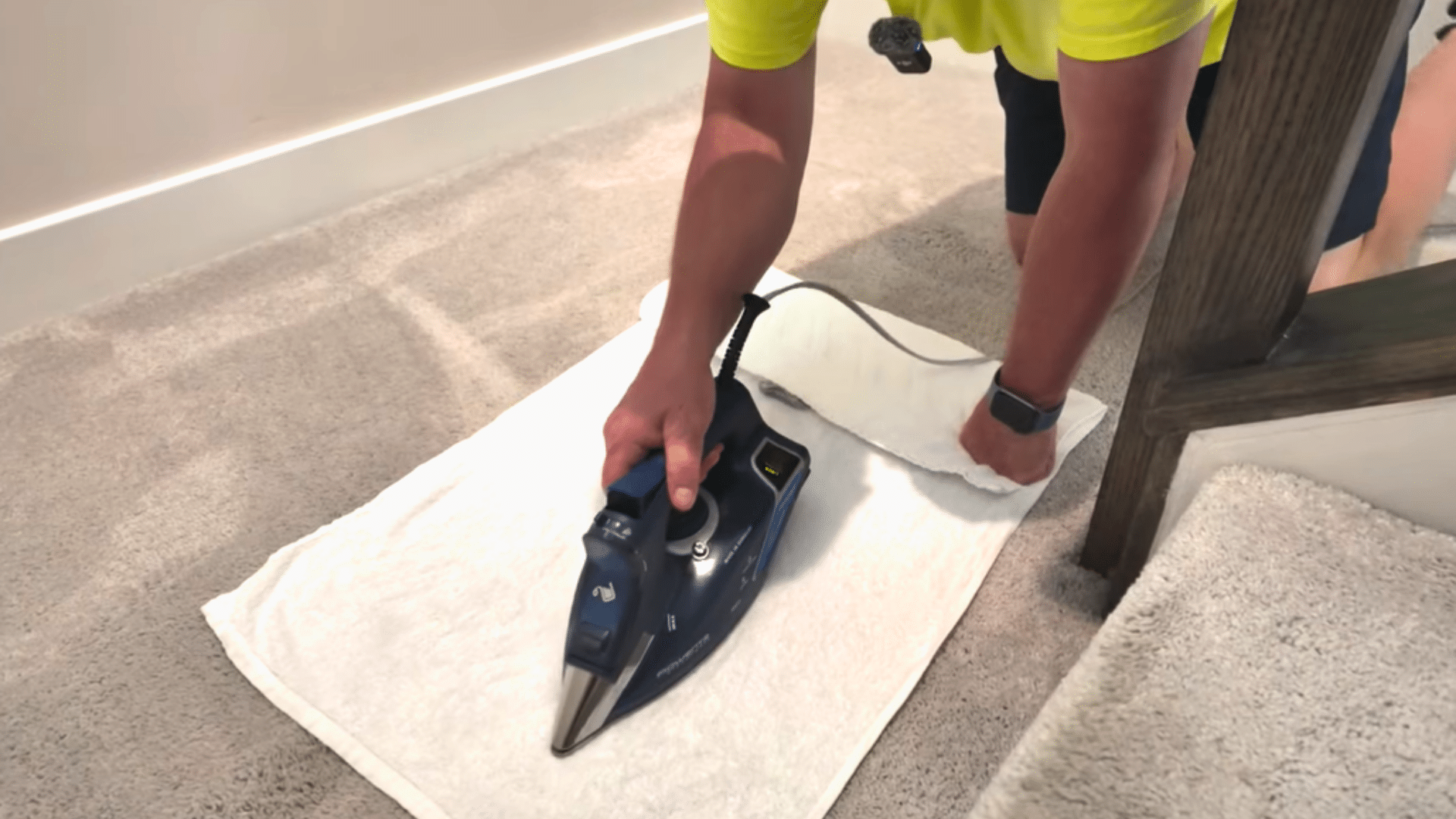 person using an iron over a white towel on beige carpet to apply steam during stain removal