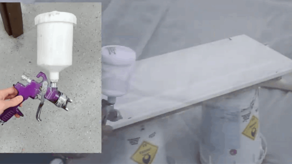 person using spray gun to apply white paint on wooden board with mist in air and tool held in hand