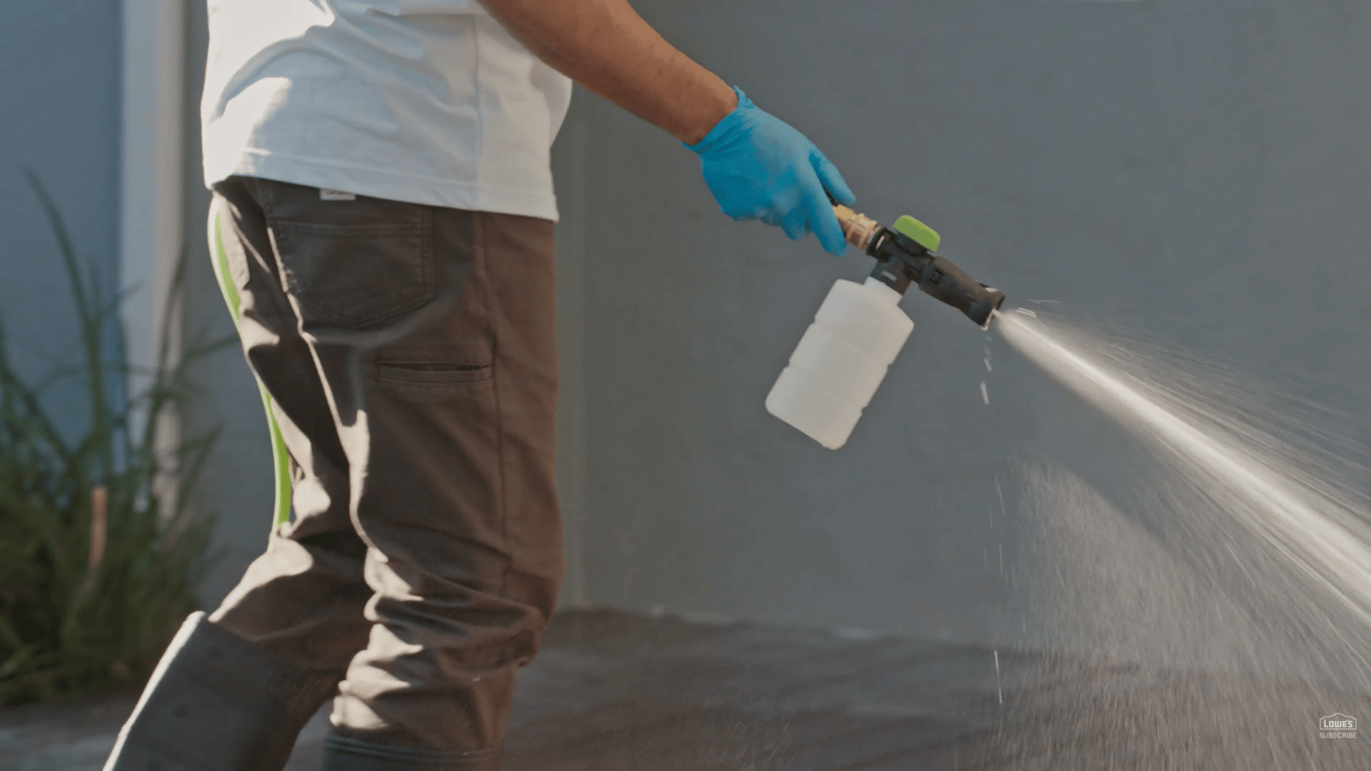 person using spray nozzle with cleaning solution while wearing gloves and boots during deck washing task