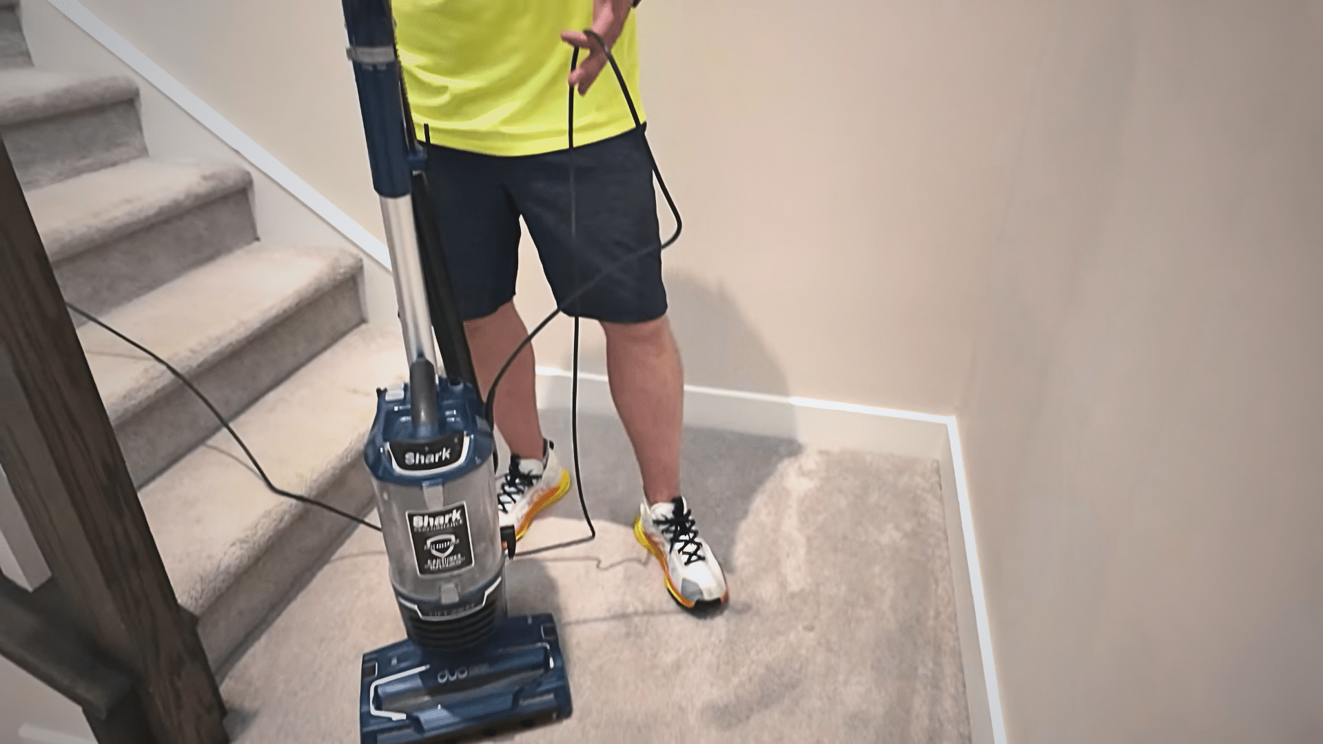 person vacuuming a light grey carpet beside stairs to remove loose dirt before treating stains