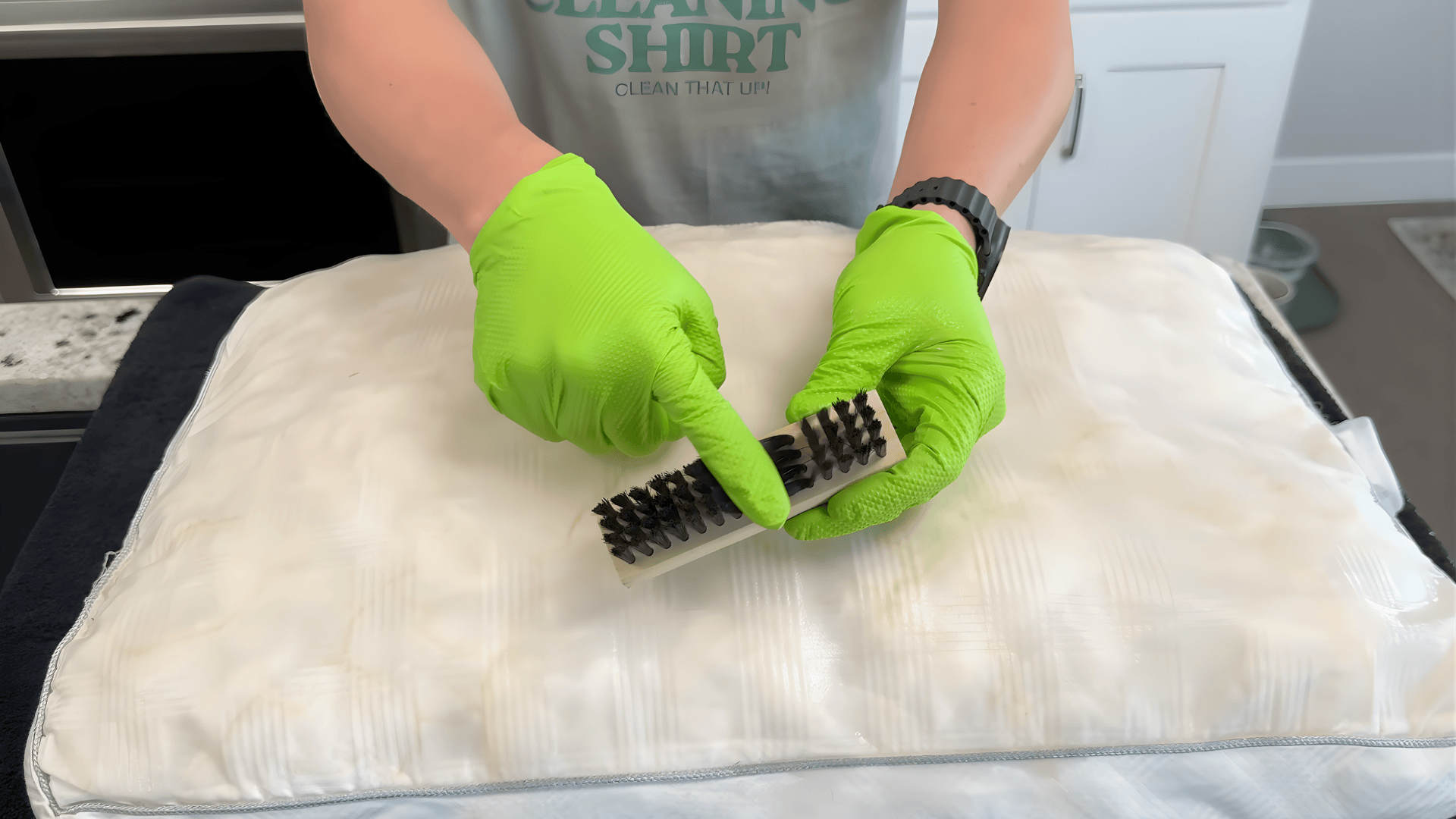 person wearing green gloves scrubbing stained pillow with brush showing how to wash pillows can you wash pillows at home
