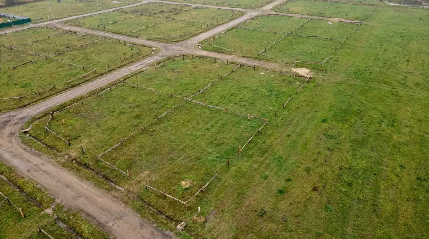 Grid-like layout of green land plots with dirt paths in rural area