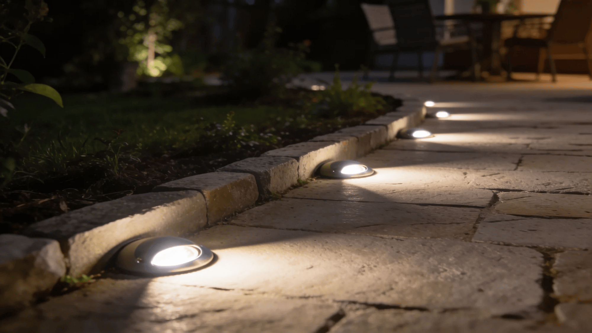 small ground lights embedded in stone path casting soft glow along garden walkway