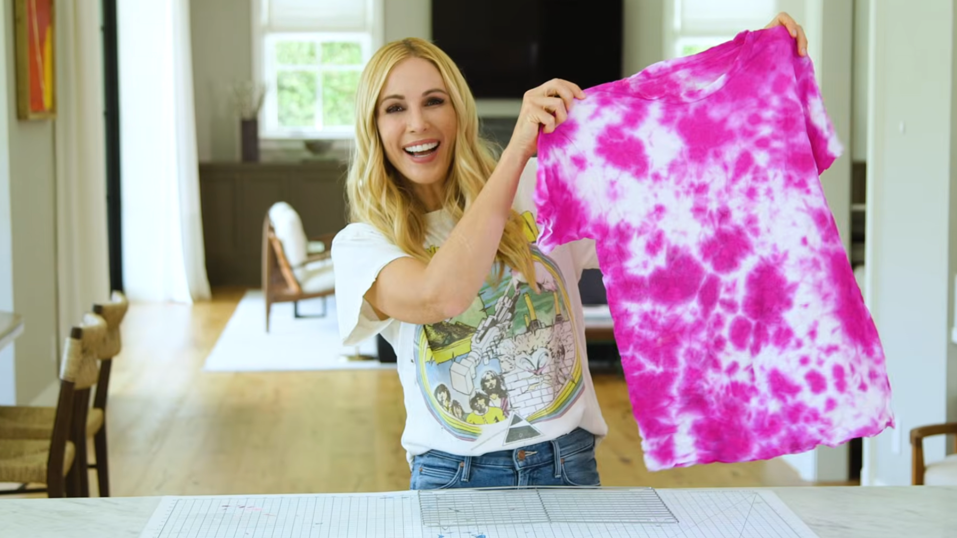 smiling woman holding a pink and white tie dye tshirt in a bright room after completing the diy craft project