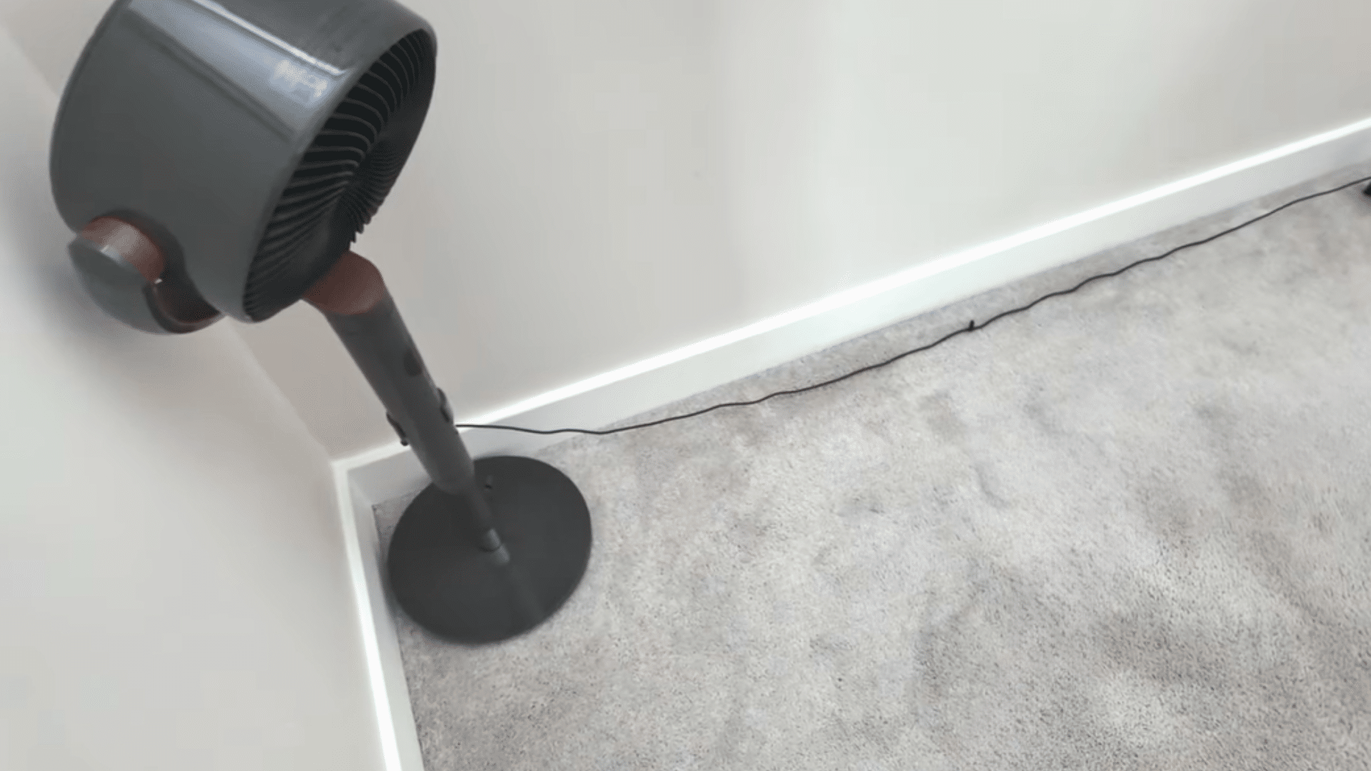 standing fan aimed at a light grey carpet near a wall to help dry the cleaned area after stain treatment