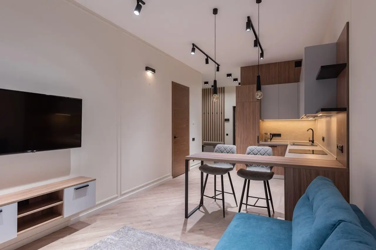 Modern open-plan living and kitchen area with gray cabinets, blue sofa, and wall-mounted TV
