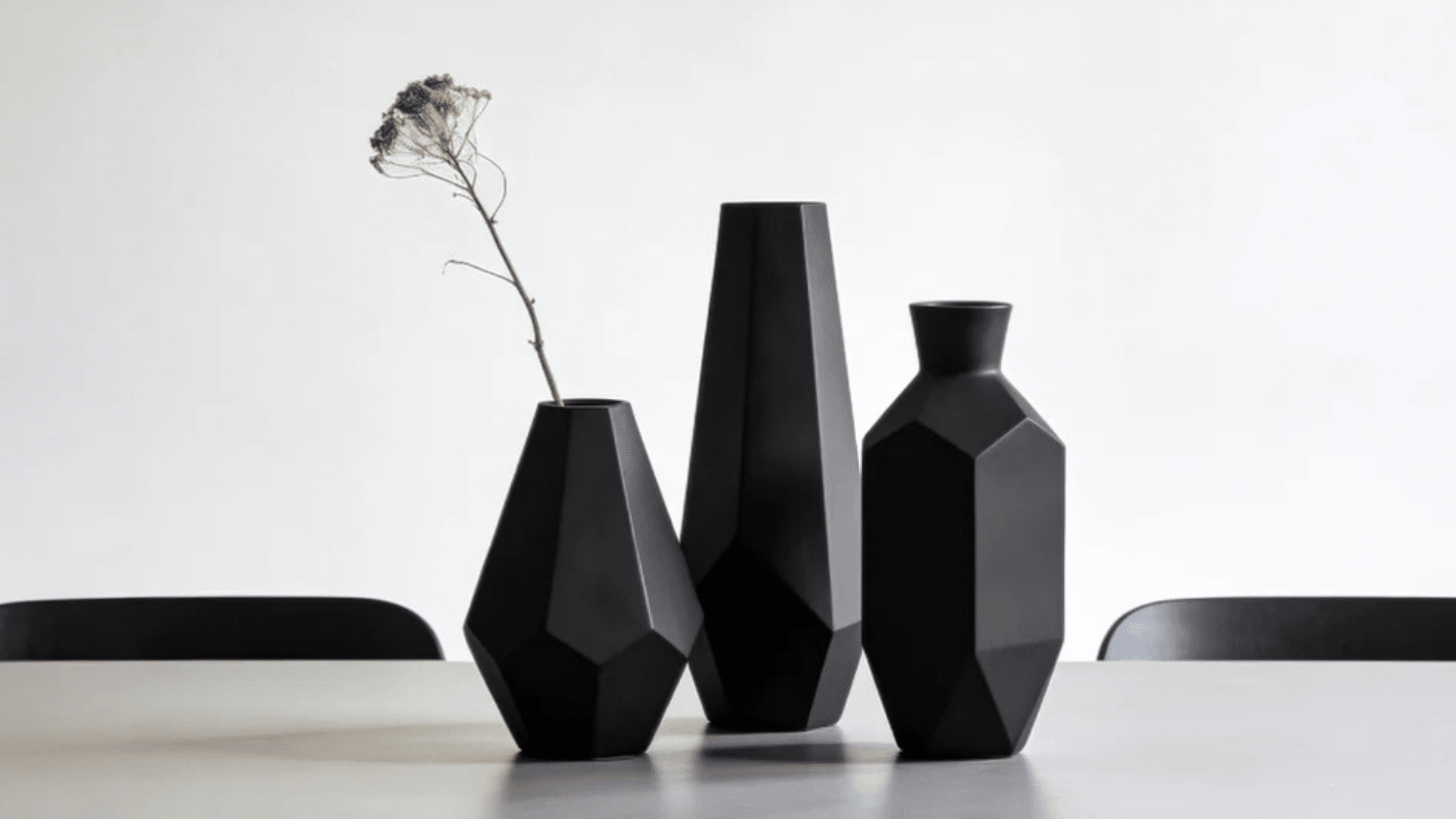 three black geometric vases on table with one dried stem in minimal bright room (1)