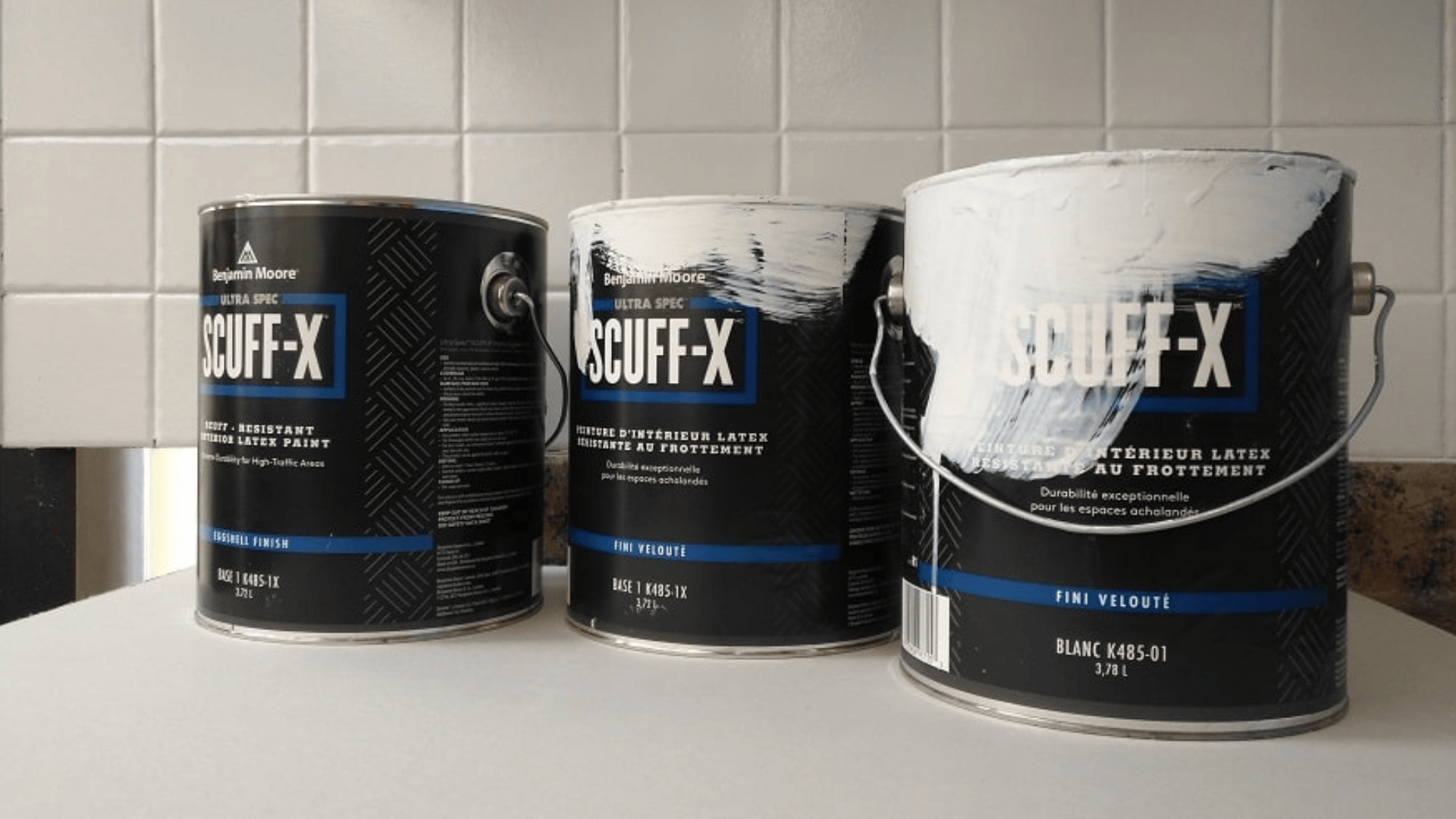 three cans of benjamin moore scuff x paint on a counter with white tile wall in background