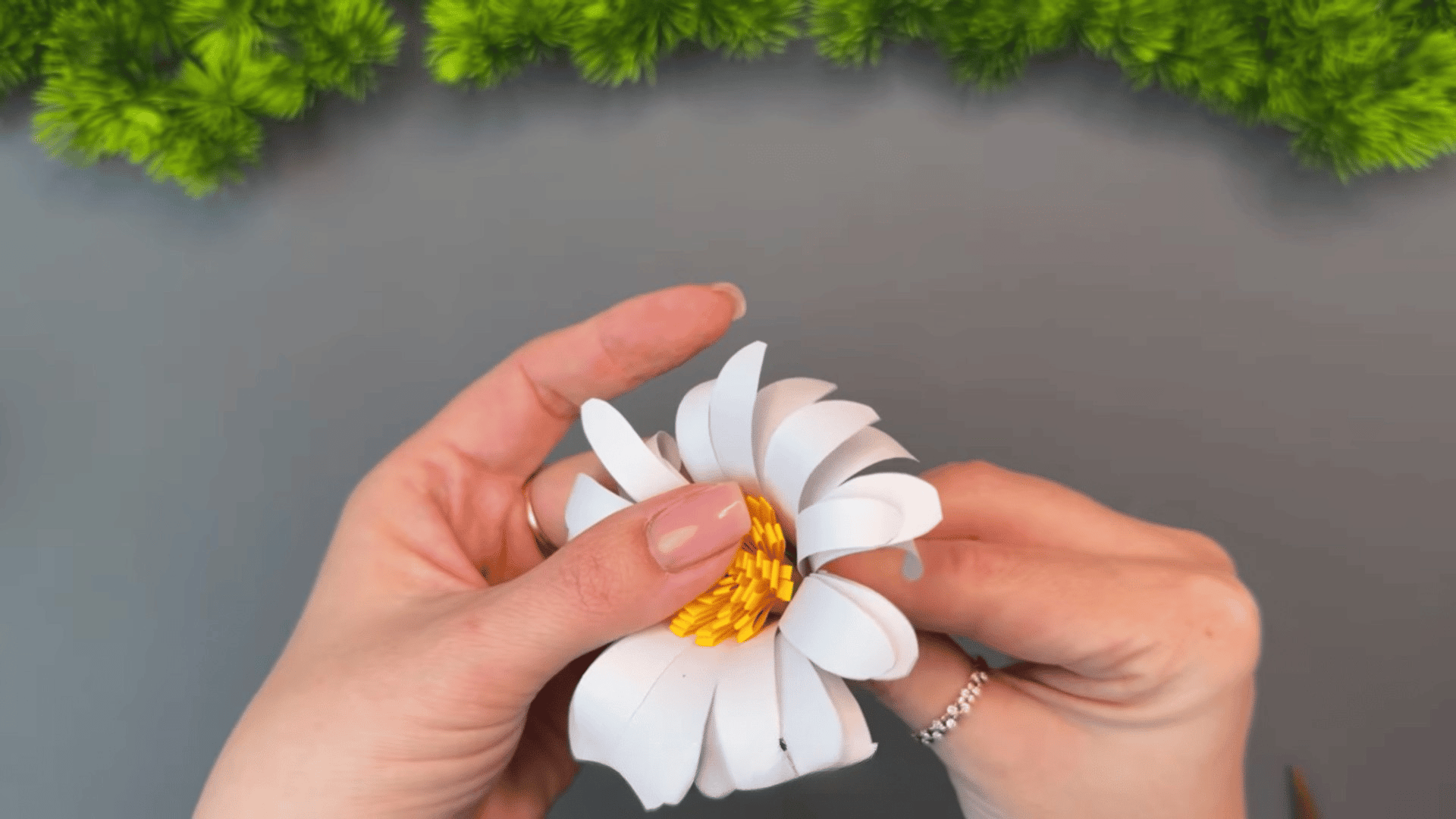 woman adjusting curled white paper petals around a textured yellow center while shaping a handmade daisy flower craft