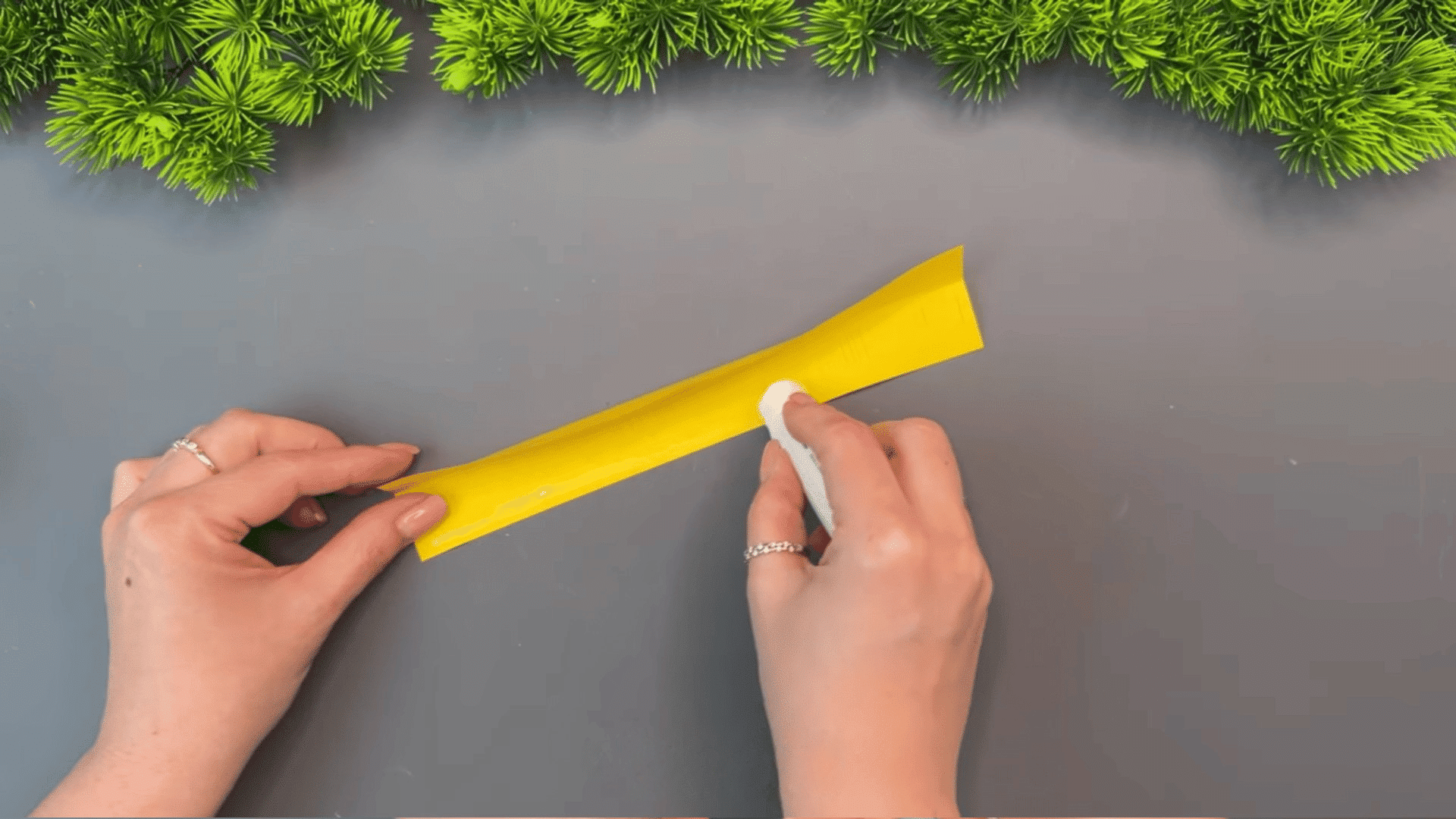 woman applying glue along a long yellow paper strip with fringe cuts while preparing materials for a paper flower craft