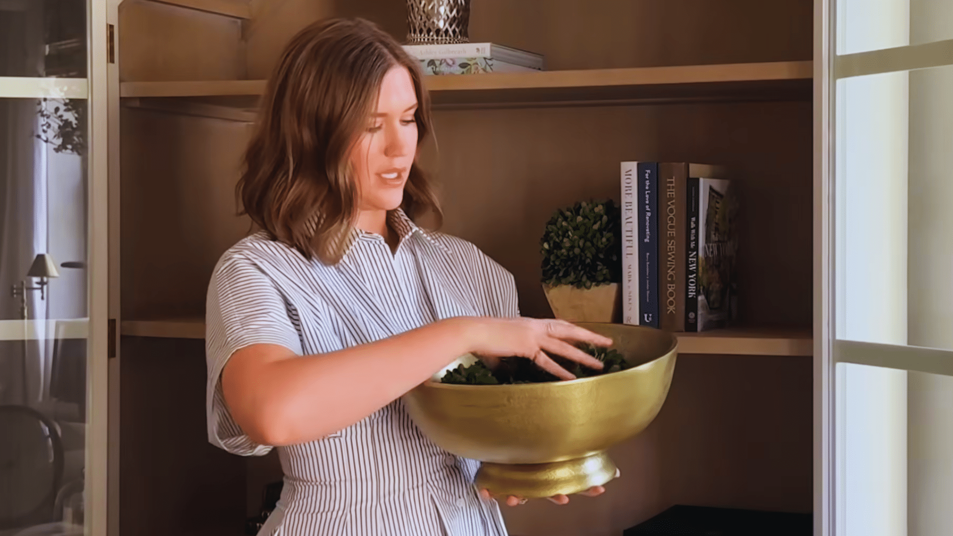 woman arranging decorative bowl with greenery on shelf to add decor pieces for interest in bookshelf
