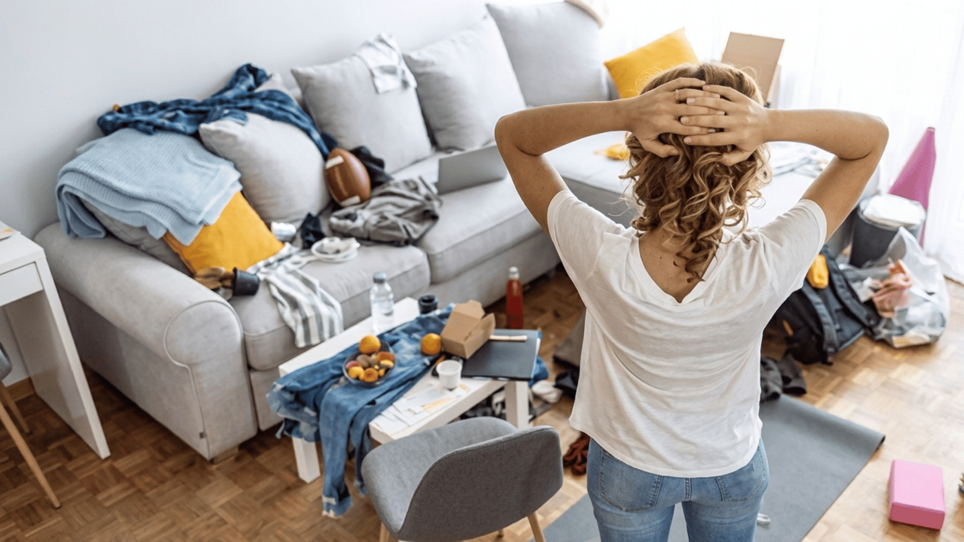 woman feeling stressed while standing in a messy living room with clothes boxes and clutter around her