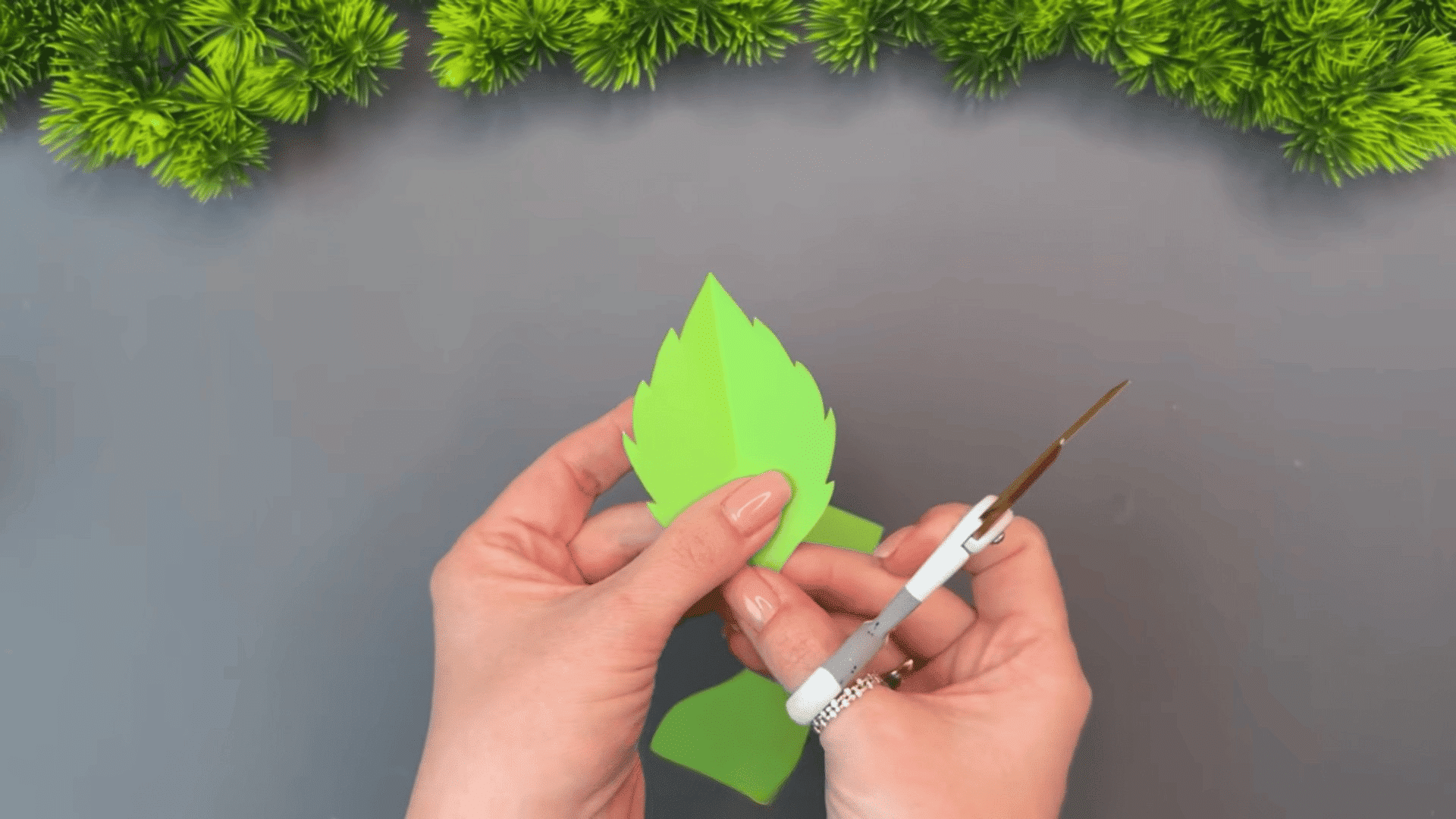 woman holding a green paper leaf and trimming the edge with scissors while making decorative leaves for a paper flower craft
