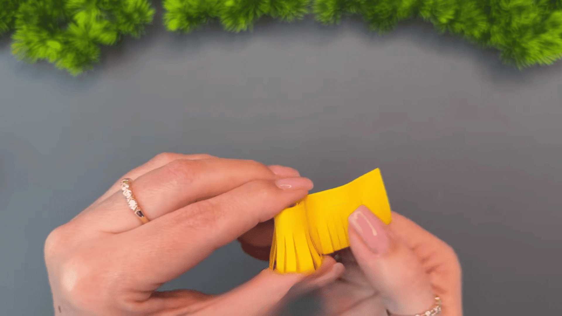 woman rolling a fringed yellow paper strip into a tight coil to create the center of a handmade paper flower