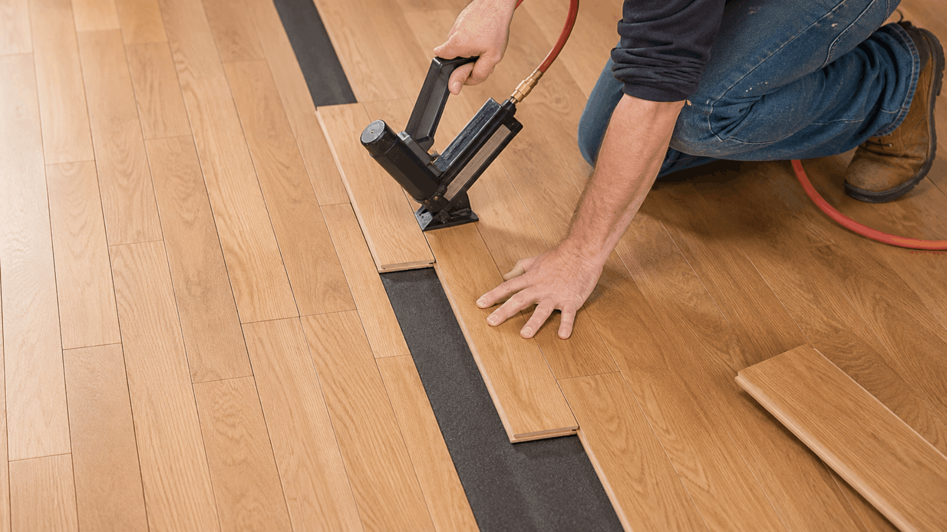worker installing engineered wood flooring with a pneumatic nailer during home renovation (1)