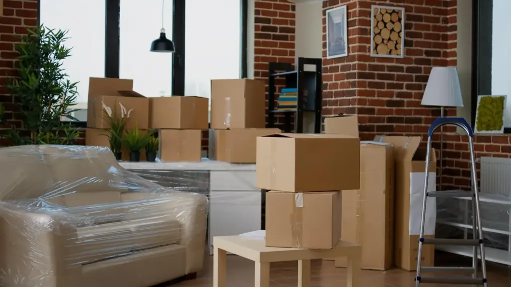 7 Signs You Need Temporary Storage Before Starting a Renovation Cardboard boxes stacked in living room with plastic-wrapped furniture and brick walls