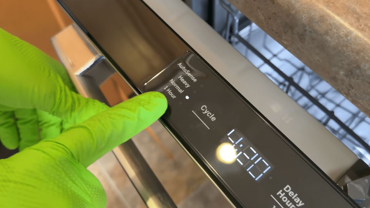 a gloved hand presses the cycle button on a modern dishwasher control panel displaying digital numbers