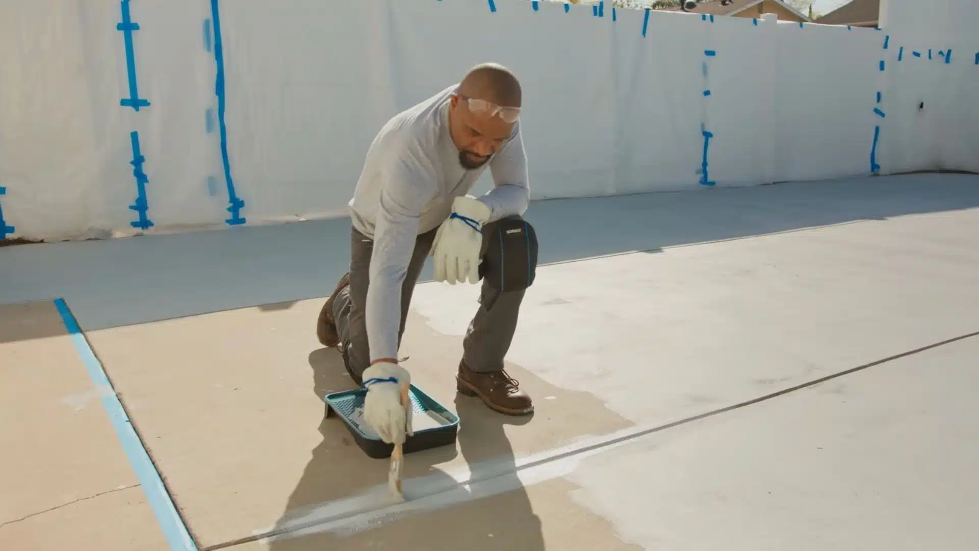 Concrete driveway being evenly stained using roller and brush in overlapping passes
