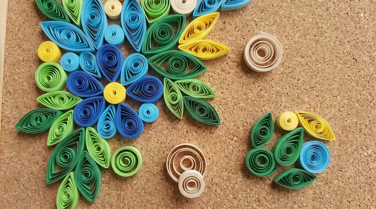 Shaped quilling coils partially arranged into a floral pattern on a cork board backing