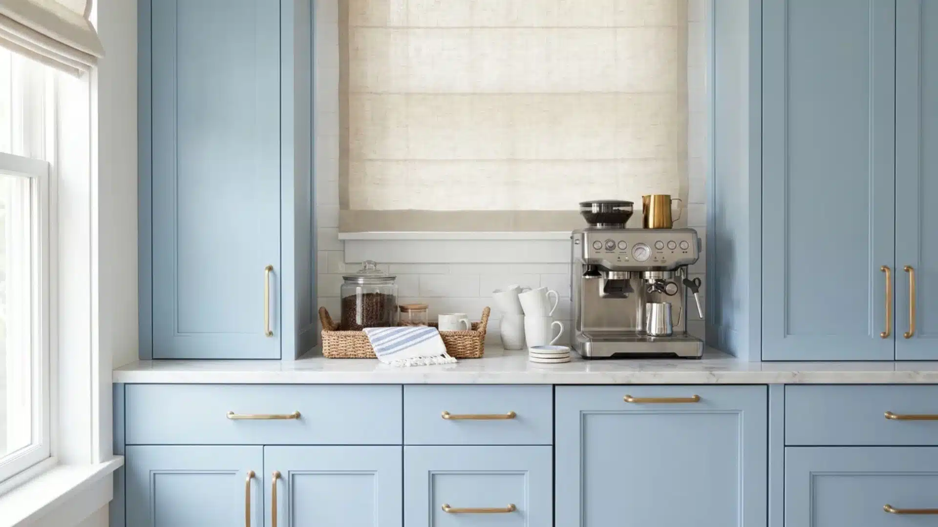 Blue shaker coffee bar with marble counter, brass hardware, espresso machine, white mugs, woven tray, and coastal light.