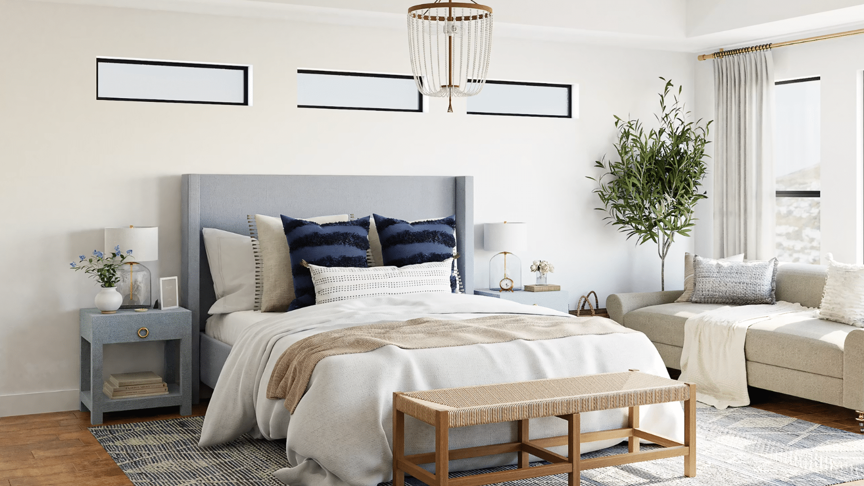 bright bedroom with upholstered bed blue accent pillows bench seating and a cozy lounge area beside tall windows and plants
