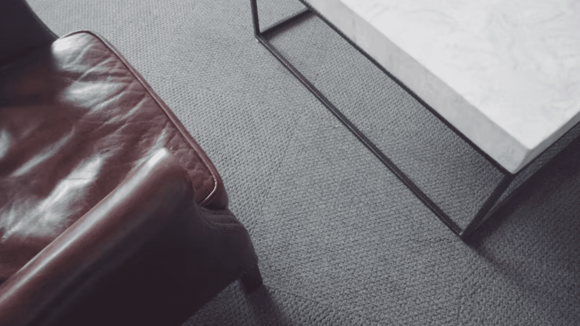 brown leather sofa beside a modern coffee table on textured gray carpet in a contemporary living room