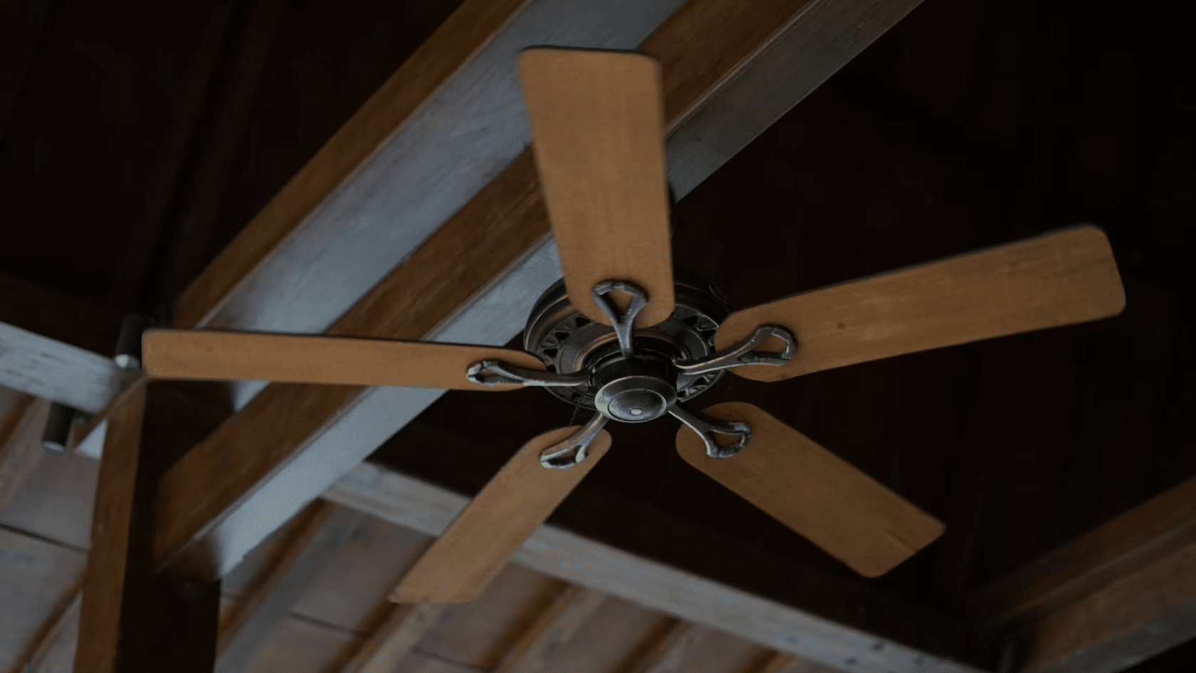 Ceiling fan mounted on exposed dark wood beams beneath a vaulted timber ceiling in rustic interior