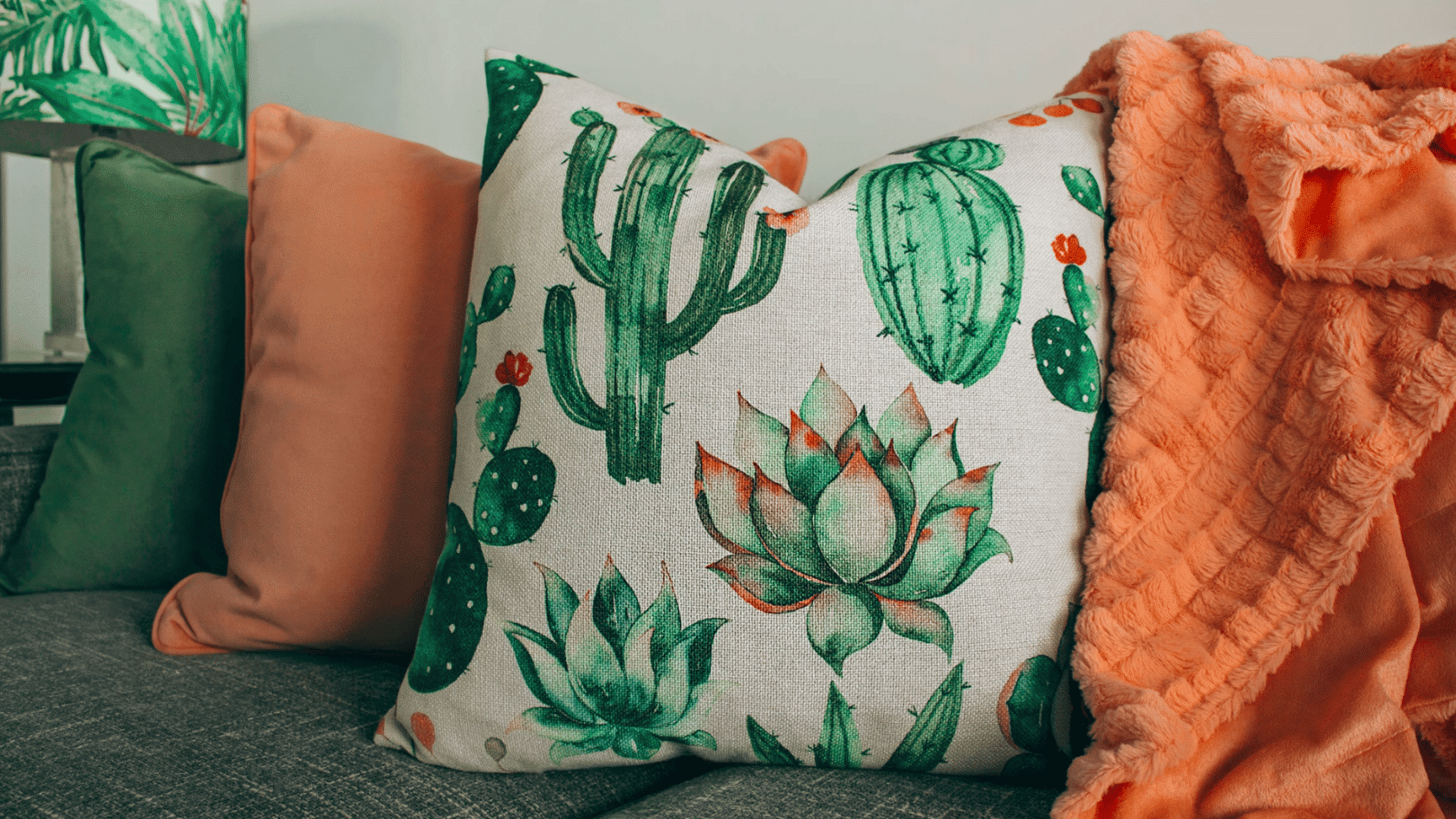 close up of decorative cactus print cushions and a soft peach throw blanket arranged on a gray sofa
